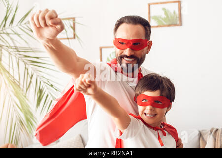 Padre e figlio in costumi superheroe a casa in piedi le mani avanti fiduciosi i superpoteri Foto Stock
