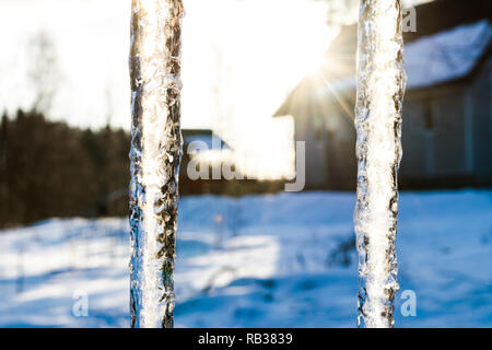Bella ghiaccioli brillare in sun contro il cielo blu. primavera paesaggio con ice ghiaccioli pendenti dal tetto della casa. La molla scende ghiaccioli gocciolamento. La fusione Foto Stock