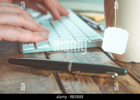 Spazio di lavoro di close-up con le mani su una tastiera e copia bianca spazio sulla tazza da tè. Il lavoro di ufficio concetto. Foto Stock