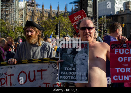 Due bianco uomo vestito come punks tenere i manifesti che attaccano il governo Tory in piazza del Parlamento durante il voto popolare di dimostrazione. Foto Stock