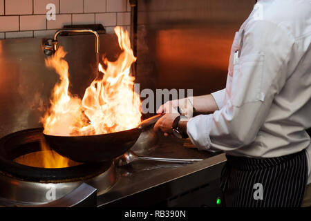 Un uomo cuochi cucina friggitrici in cucina il fuoco. Processo di cottura di cibo nel ristorante. Foto Stock