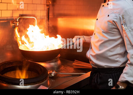 Un uomo cuochi cucina friggitrici in cucina il fuoco. Processo di cottura di cibo nel ristorante. Foto Stock