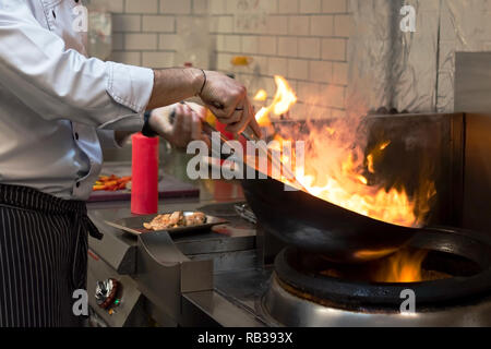 Un uomo cuochi cucina friggitrici in cucina il fuoco. Processo di cottura di cibo nel ristorante. Foto Stock