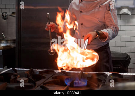 Un uomo cuochi cucina friggitrici in cucina il fuoco. Processo di cottura di cibo nel ristorante. Foto Stock