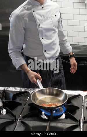 Un uomo cuochi cucina friggitrici in cucina il fuoco. Processo di cottura di cibo nel ristorante. Orientamento verticale Foto Stock