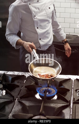 Un uomo cuochi cucina friggitrici in cucina il fuoco. Processo di cottura di cibo nel ristorante. Orientamento verticale Foto Stock