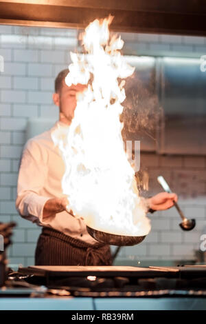 Un uomo cuochi cucina friggitrici in cucina il fuoco. Processo di cottura di cibo nel ristorante. Foto Stock