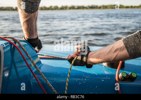Silhouette di marinai mani su una fune del verricello a bordo di una barca a vela al tramonto. Girato con una messa a fuoco selettiva. Foto Stock