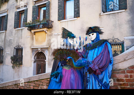 Venezia, Italia - 10 Febbraio 2018: matura in maschere bianche e viola e blu costumi su strada durante il carnevale Foto Stock