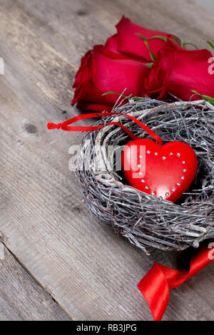 Decorazione di festa. cuore rosso in un nido, rose rosse su un vecchio sfondo di legno Foto Stock