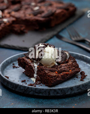 Brownie con oreo e gelato alla vaniglia in una piastra di colore blu su sfondo blu close-up Foto Stock