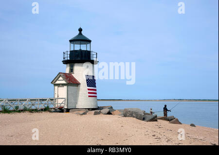 Pesca al largo della spiaggia di sabbia da Brant Point lighthouse a Nantucket Island in Masssachusetts. Il faro rotante è avvolto in una bandiera americana. Foto Stock