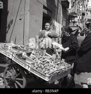 Degli anni Cinquanta, una signora acquistare verdure da una donna napoletana portatile del mercato al di fuori di stallo in una strada laterale, Napoli, Italia Foto Stock