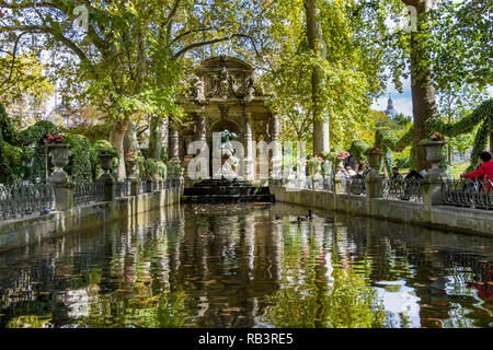 Persone sedute presso lo stagno alla Fontana dei Medici o Fontaine de Medicis, una fontana monumentale, in una giornata estiva nel Jardin du Luxembourg, Parigi Foto Stock