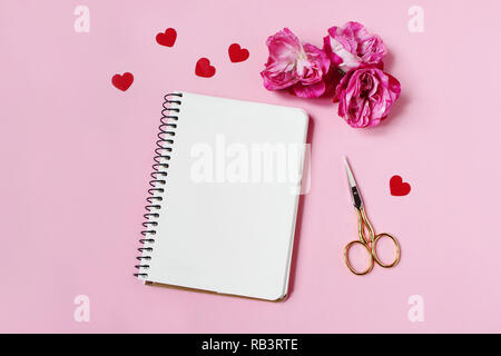 Matrimoni, compleanni o Valentines stationery mockup scena. Le rose rosa, rosso forma di cuore carta coriandoli, vuoto portatile e forbici d'oro su sfondo rosa. Appartamento laico, vista dall'alto. Foto Stock