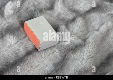 Piccolo matchbox confezione regalo con uno arancione sul lato grigio argento soffice pelliccia di sfondo coperta Foto Stock
