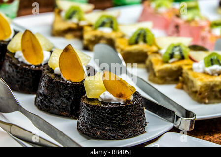 Chiudere il lotto dessert deliziosi dolci di pasticceria pasticcini in una fila. Fresche, multicolore, colorata, verde, giallo, bianco e rosa bacca dolce dessert, essere Foto Stock