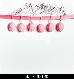 Pasqua sfondo con appesa rosa pastello uova di Pasqua su nastro con fiori di colore bianco. Pasqua confine con copia spazio per il vostro design Foto Stock