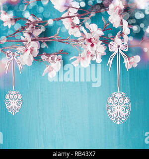 Dipinto di appendere le uova di Pasqua in primavera la fioritura dei ciliegi si dirama in turchese sfondo blu. Pasqua biglietto di auguri Foto Stock