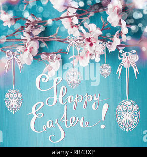 Felice Pasqua testo scritte con molla blossom rami e dipinto di appendere le uova di Pasqua al turchese sfondo blu. Pasqua biglietto di auguri Foto Stock