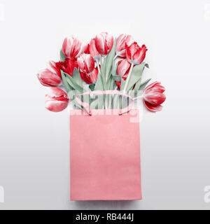 Tulipani rossi bouquet in carta shopping bag su sfondo grigio chiaro. Molla di festosa mazzo di fiori. Regalo floreale che compongono. Vacanze di primavera , saluto Foto Stock