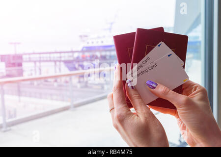 Primo piano della donna bella mano che tiene il passaporto e carta di imbarco biglietti al terminal aeroportuale. I viaggi e le vacanze concetto. Il terminale lounge. Vuoto sp Foto Stock