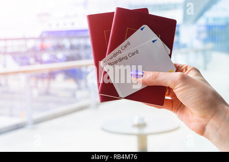 Primo piano della donna bella mano che tiene il passaporto e carta di imbarco biglietti al terminal aeroportuale. I viaggi e le vacanze concetto. Il terminale lounge. Vuoto sp Foto Stock