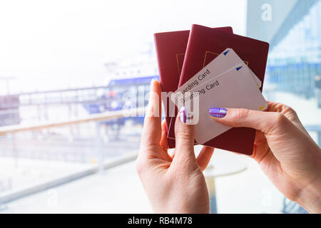 Primo piano della donna bella mano che tiene il passaporto e carta di imbarco biglietti al terminal aeroportuale. I viaggi e le vacanze concetto. Il terminale lounge. Vuoto sp Foto Stock