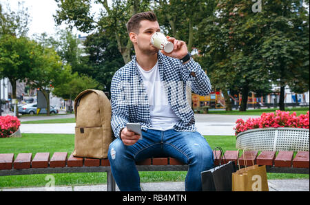 Uomo con mobile di bere il caffè seduta su una panchina Foto Stock