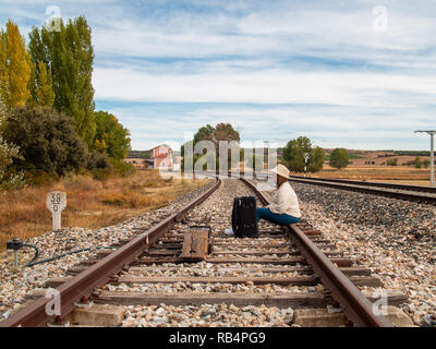 Un triste donna bionda con un cappello di paglia seduti sui binari del treno con una valigia in autunno Foto Stock