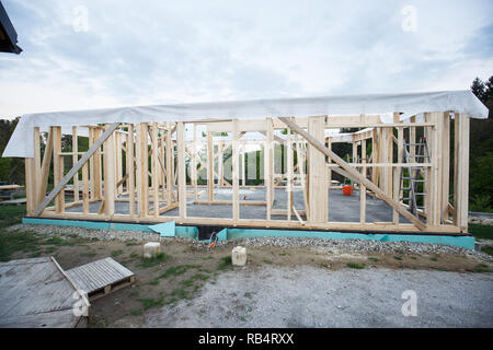 Telaio di legno casa in costruzione, coperto con tyvec home wrap. Processo di costruzione, sito in costruzione, falegnameria, edificio asciutto il concetto di settore. Foto Stock