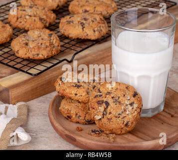 Farina di avena raisin cookie di dado e un bicchiere di latte sul piatto di legno con i cookie su un raffreddamento per rack in background Foto Stock