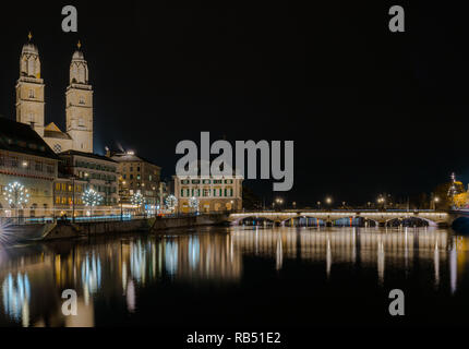 Il paesaggio di Zurigo di notte con il fiume Limmat e il Grossmuenster cattedrale e il ponte con riflessi di luci in primo piano Foto Stock