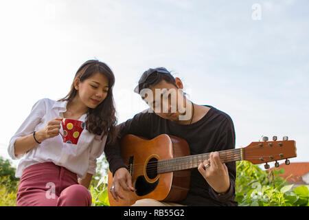 Coppie di giovane uomo asiatico e la donna rilassante a suonare la chitarra in posizione di parcheggio Foto Stock