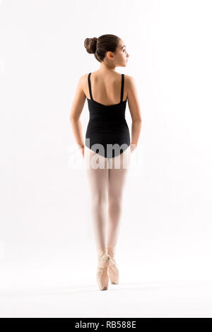 Vista posteriore di una giovane ballerina in un nero leotard posa sul pointe equilibratura su le punte delle sue dita isolato su bianco Foto Stock