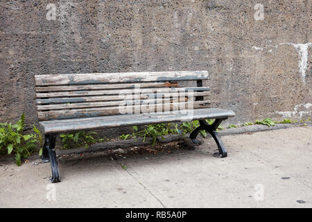 Il vecchio obsoleto panca in legno sul marciapiede davanti ad un muro di cemento Foto Stock