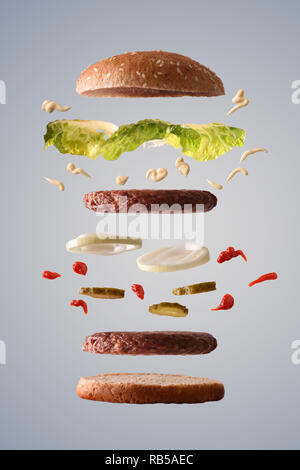 Doppio hamburger con lattuga cipolla e sottaceti flottante con ingredienti ripartiti in parti sul gradiente grigio Sfondo isolato. Vista frontale. Verti Foto Stock