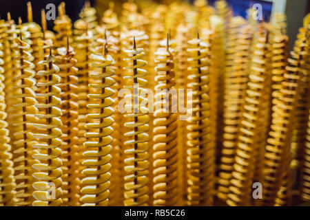 Spirale di patate fritte, su bastoni di legno a spirale. La vendita di prodotti alimentari al mercato. Malsana alimenti fritti. Cucina di strada, una spirale di patate fritte su un bastone Foto Stock