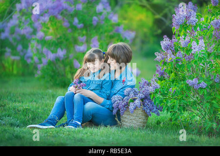 Carino adorabile madre di beautifull lady donna mom con brunette girl figlia in prato di lilla bush.Persone in jeans usura Foto Stock