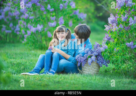 Carino adorabile madre di beautifull lady donna mom con brunette girl figlia in prato di lilla bush.Persone in jeans usura Foto Stock