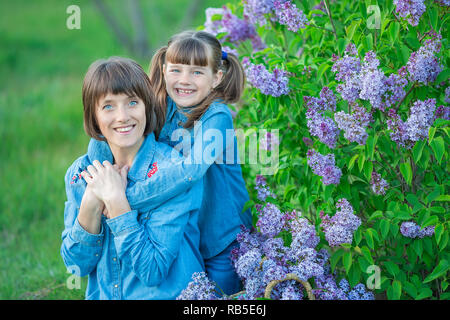 Carino adorabile madre di beautifull lady donna mom con brunette girl figlia in prato di lilla bush.Persone in jeans usura Foto Stock