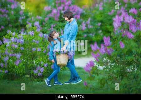 Carino adorabile madre di beautifull lady donna mom con brunette girl figlia in prato di lilla bush.Persone in jeans usura Foto Stock