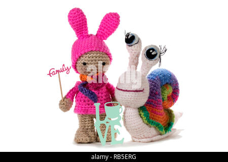 Ragazza a crochet Holding firmano la famiglia e crochet lumaca arcobaleno da segno di amore, su sfondo bianco. Amigurumi. Fatte a mano Foto Stock