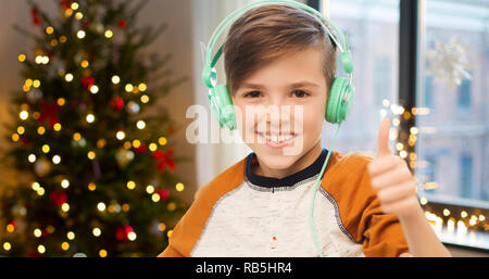 Ragazzo in auricolari che mostra i pollici fino a Natale Foto Stock