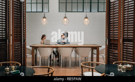 Due giovani creativi avente una riunione nella sala riunioni privata in un cafe con il computer portatile Foto Stock