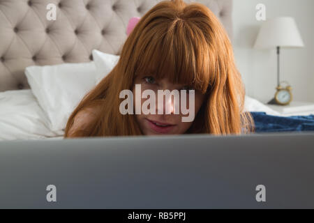Donna che utilizza computer portatile in camera da letto a casa Foto Stock