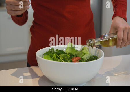Donna versando olio di cottura su vegetali in cucina Foto Stock