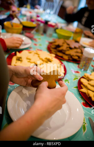 Close up kids' mani tenendo a casa gingerbread man biscotto a una tabella durante un cookie workshop di decorazione a casa durante il periodo di Natale Foto Stock
