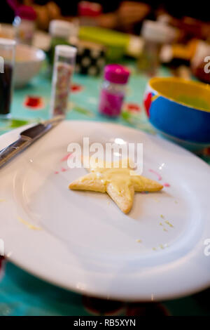 Mezza decorate in casa cookie conformata come una stella ricoperto di crema colorata ciliegina su una piastra bianca circondata da altri ingredienti a natale Foto Stock