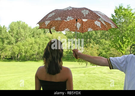 Man tenere l'ombrello per una signora di fornire qualche ombra Foto Stock